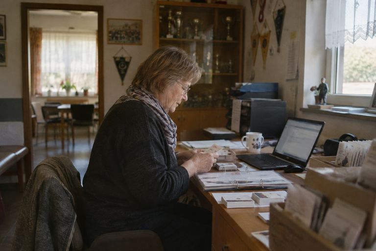 Ein Vorstandsmitglied sortiert in der Geschäftsstelle des Vereins Karteikarten und Mitgliedsausweise, daneben liegen ein Ordner und ein aufgeklappter Laptop.